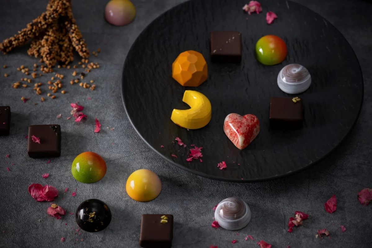 黒い皿の上と周囲に、色とりどりの美しいチョコレートが並べられています