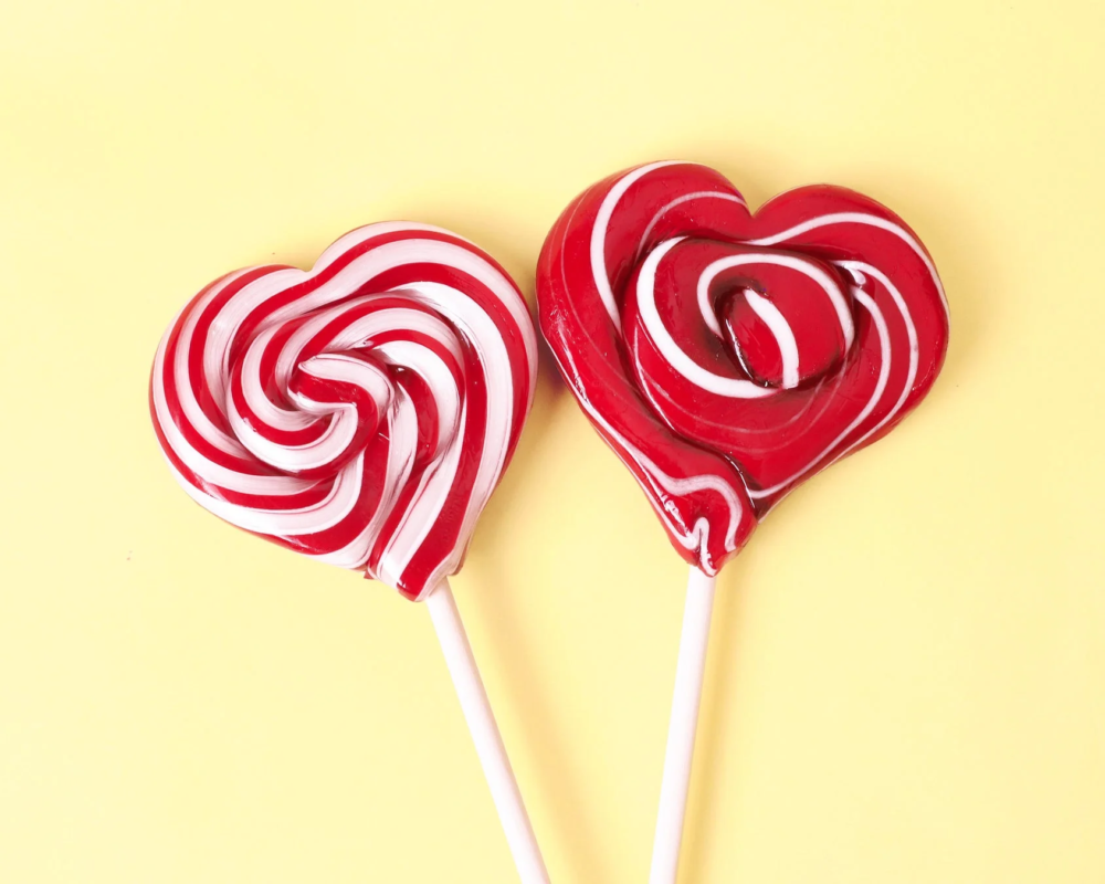 黄色い背景に、赤と白の渦巻き模様のハート型ロリポップが2つ