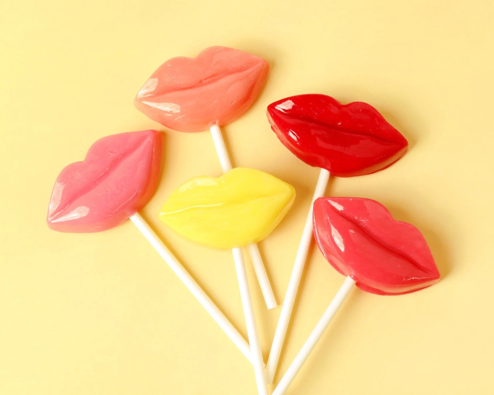 明るい黄色の背景に、赤、ピンク、黄色の唇の形をしたロリポップが5本