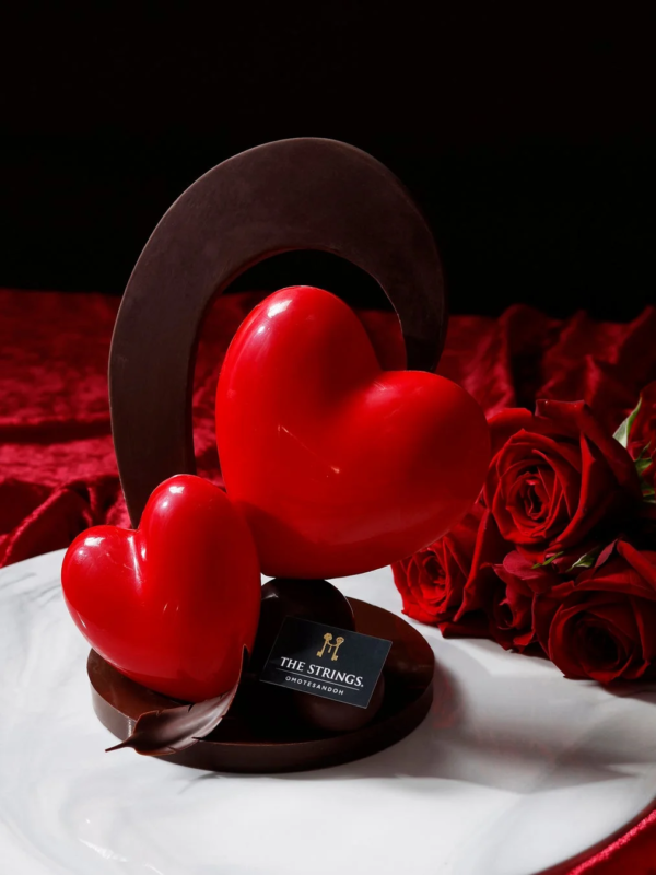 赤いハート形のチョコレート細工が特徴的なデザートです。背景には赤いバラが添えられ、バレンタインデーなどのロマンチックな雰囲気を演出しています。