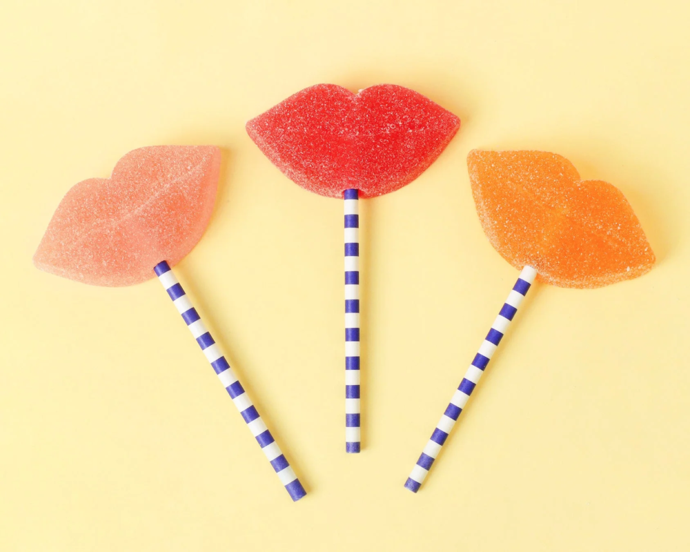 黄色い背景に、赤、ピンク、オレンジ色の唇型キャンディが3つ
